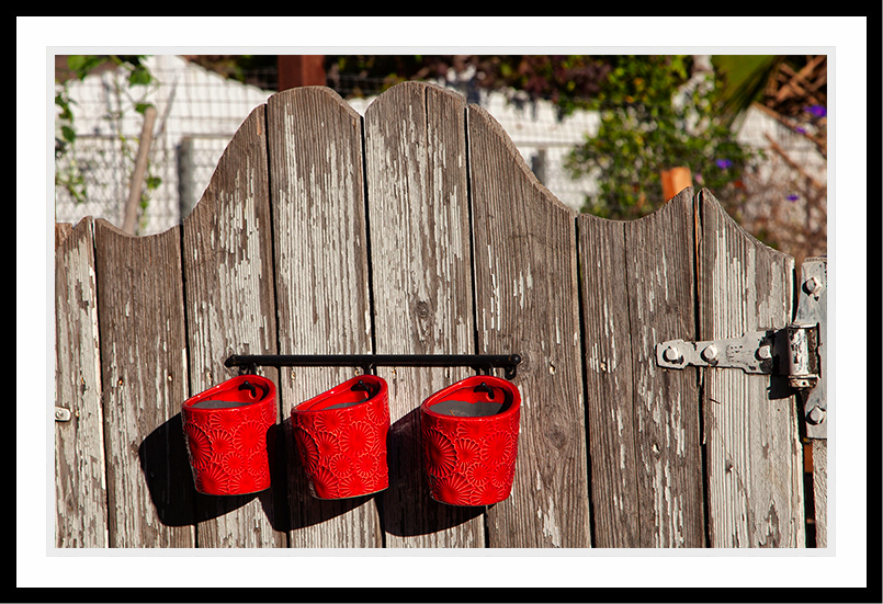Three red pots hanging on a gate.